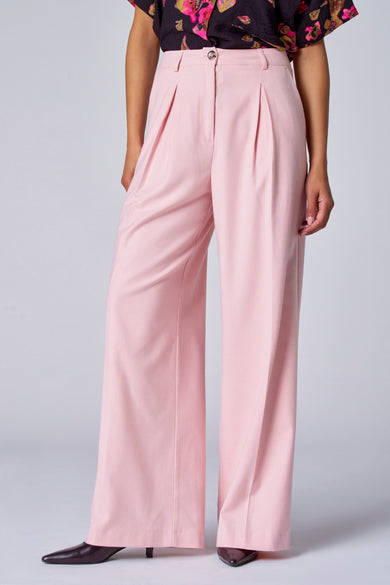 Jean taille basse rose d'Astrid Black Label, avec des plis et une large ce, combiné à une blouse fleurie et des chaussures à bouts pointus.