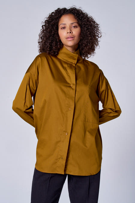 Groene blouse met lange mouwen van Astrid Black Label, met knoopsluiting en een borstzak, gedragen met een zwarte broek.
