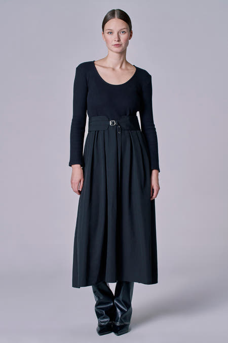 Robe noire à longues manches d'Astrid Black Label, avec une ceinture à la taille et des bottes en cuir.