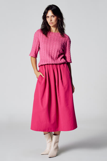Roze kleedje met korte mouwen van Astrid Black Label, met kabelpatroon en midi rok, gedragen met crèmekleurige laarzen.
