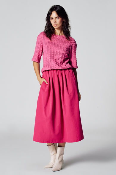 Robe rose à manches courtes d'Astrid Black Label, avec un motif côtelé et une jupe midi, portée avec des bottes crème.