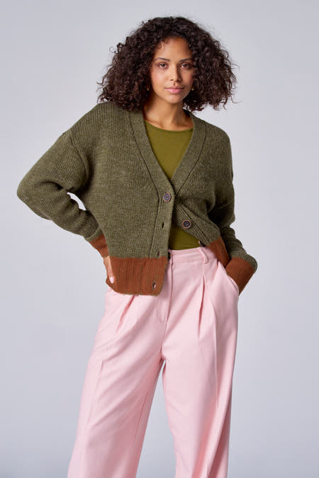 Groene trui met V-hals van Astrid Black Label, gedragen met een olijfgroen shirt en roze pantalon.