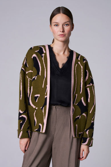 Groene korte jas van Astrid Black Label met een abstract zwart en roze patroon, gedragen met een zwarte top en bruine broek.
