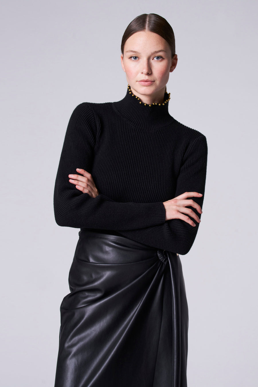 Collier noir Astrid Black Label, avec des strass dorés le long du col et une texture à larges bretelles, associé à une jupe en cuir noir.