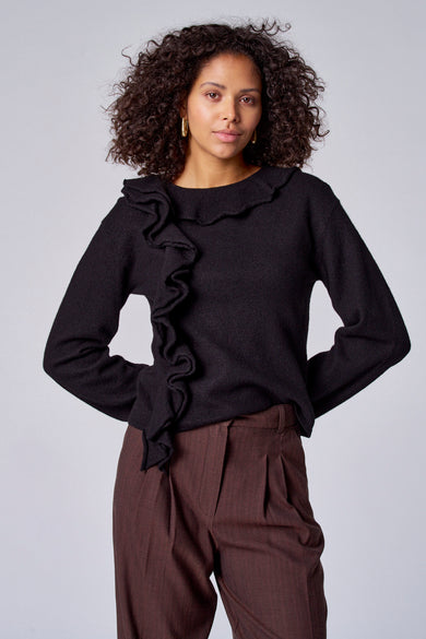 Pull noir à col montant d'Astrid Black Label, avec des plis décoratifs à l'avant et associé à un pantalon marron.
