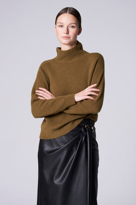 Groene coltrui van Astrid Black Label, met gekruiste armen gedragen boven een zwarte leren rok met knoopdetail.
