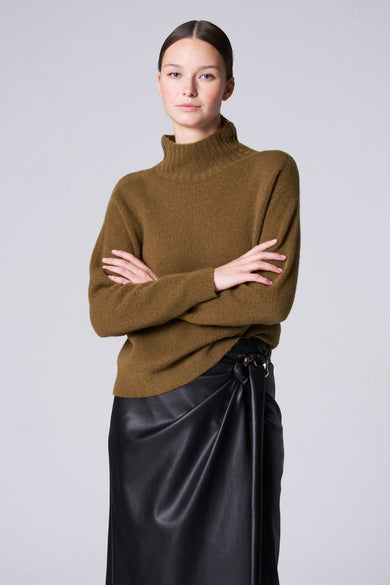 Groene coltrui van Astrid Black Label, met gekruiste armen gedragen boven een zwarte leren rok met knoopdetail.
