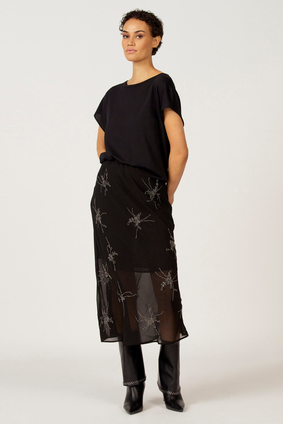 Zwarte trui met ronde hals van Astrid Black Label, gecombineerd met een lange rok met spinnenapplicaties en zwarte laarzen.
