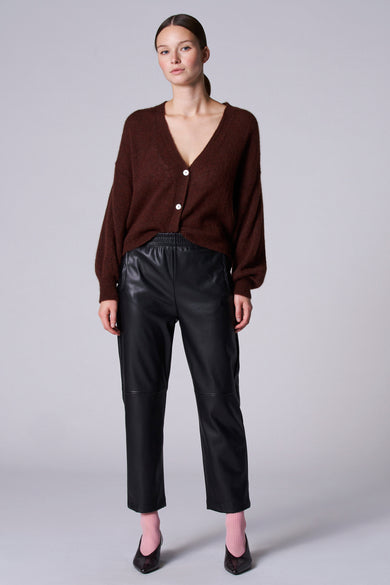 Bruin gilet van Astrid Black Label, met lange mouwen en witte knopen, gedragen met zwarte leren broek.