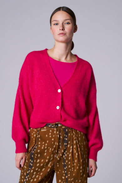 Roze gilet van Astrid Black Label, met lange mouwen en knoopsluiting, gecombineerd met een bruine broek met stippenpatroon.