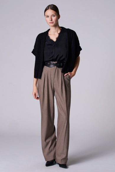 Zwarte singlet van Astrid Black Label, met kanten details bij de V-hals, gedragen onder een gebreid vest en een bruine pantalon met riem.