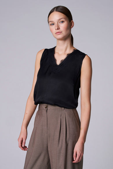 Zwarte singlet van Astrid Black Label met kanten V-hals, gecombineerd met een bruine, geplooide pantalon.
