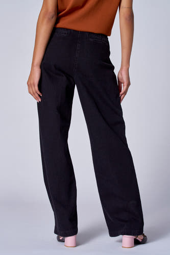 Jean délavé noir d'Astrid Black Label, vu de derrière, associé à un t-shirt marron et des baskets roses.