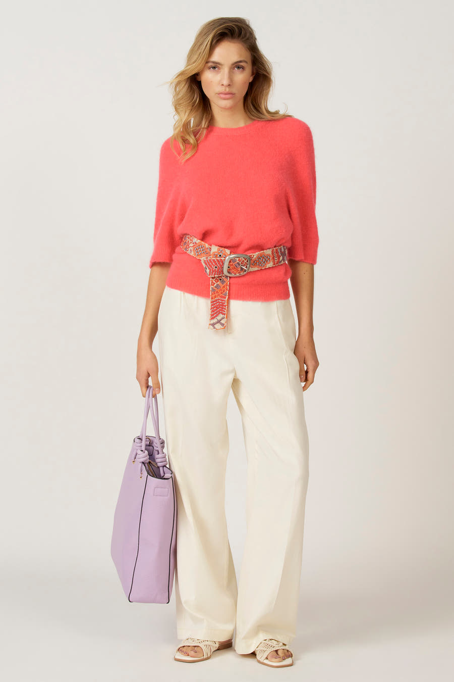 T-shirt rose avec col rond d'Astrid Black Label, associé à une ceinture dessinée, un pantalon blanc et un sac violette.