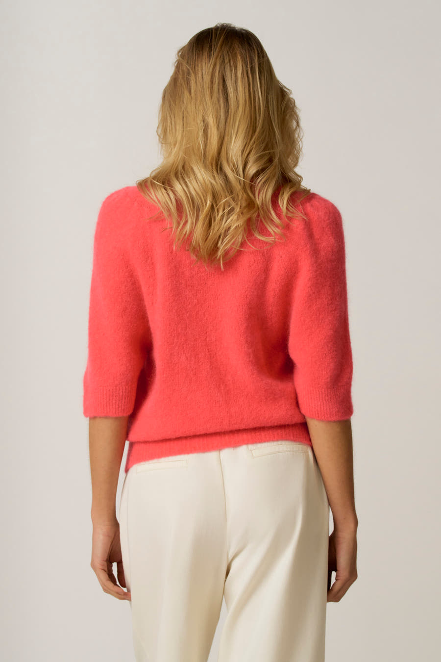 Roze trui met ronde hals van Astrid Black Label, gezien van achteren, met crèmekleurige pantalon.
