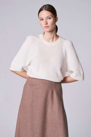 Witte trui met ronde hals van Astrid Black Label, met korte mouwen en een bruine rok.
