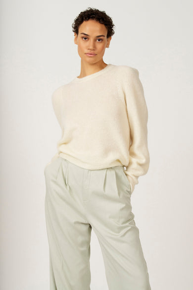 Ecru trui met ronde hals van Astrid Black Label, gedragen met lichtgroene pantalon, met de handen in de zakken.
