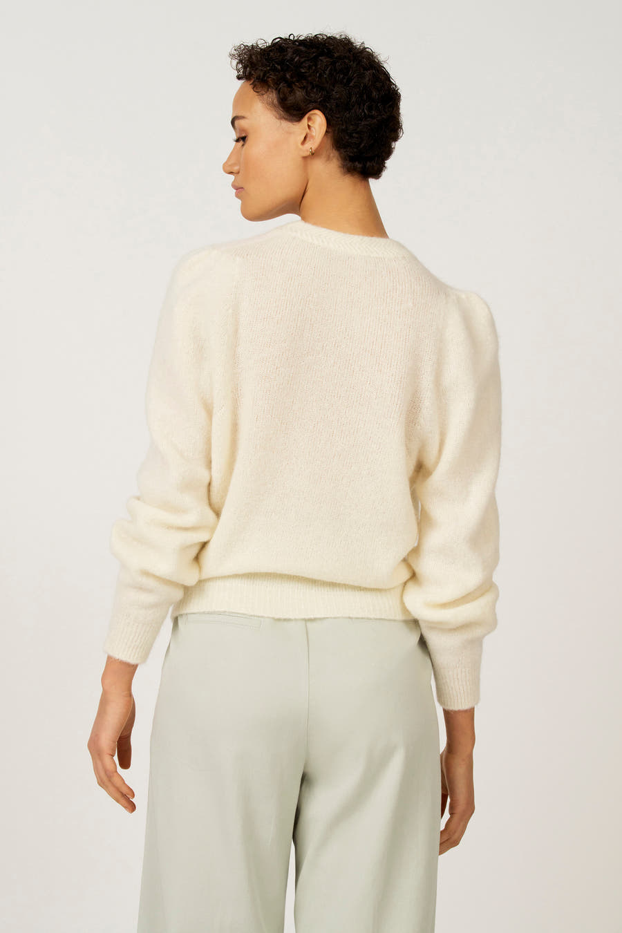Ecru trui met ronde hals van Astrid Black Label, gezien van achteren, met pofmouwen en gecombineerd met een groene broek.
