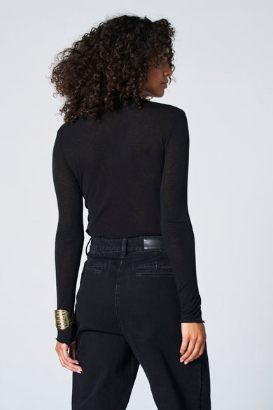 T-shirt noir à manches longues d'Astrid Black Label, porté avec un bracelet en or et des jeans noirs.