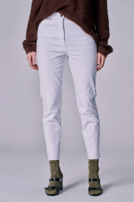 Witte jeans 7/8 van Astrid Black Label, met een gerafelde zoom, gecombineerd met een bruine trui en glinsterende sokken met sandalen.