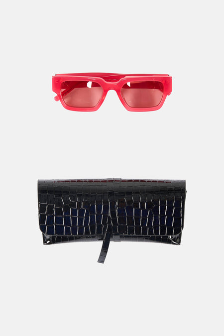 Roze zonnebril van Astrid Black Label, met een zwarte clutch met krokodillenpatroon eronder, op een witte achtergrond.
