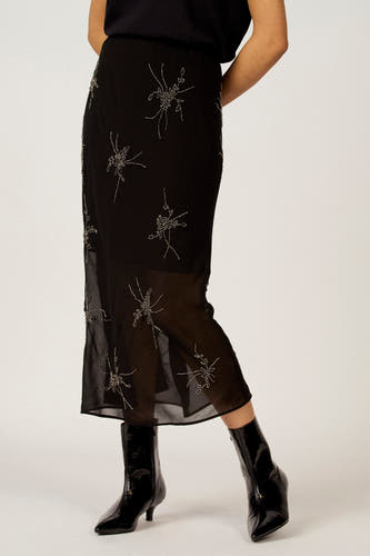 Zwarte rok van Astrid Black Label met zilverkleurige bloemmotieven, gecombineerd met zwarte, glanzende enkellaarsjes.
