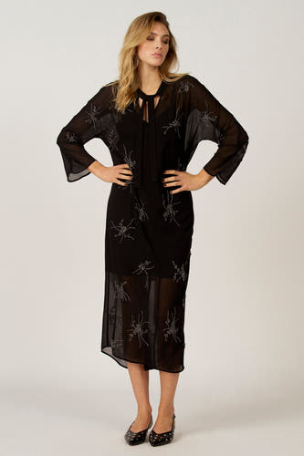 Zwarte jurk met lange mouwen van Astrid Black Label, versierd met zilverkleurige details en een transparante stof.