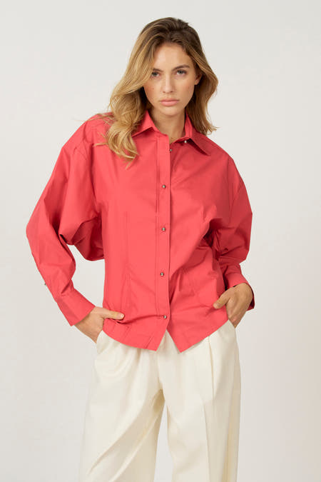 Roze hemd met lange mouwen van Astrid Black Label, met zilveren knopen en gedragen met een witte broek.
