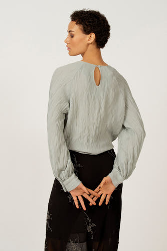 Blauw blouse met lange mouwen van Astrid Black Label, met een subtiele plooistructuur en knoopdetail aan de achterkant.

