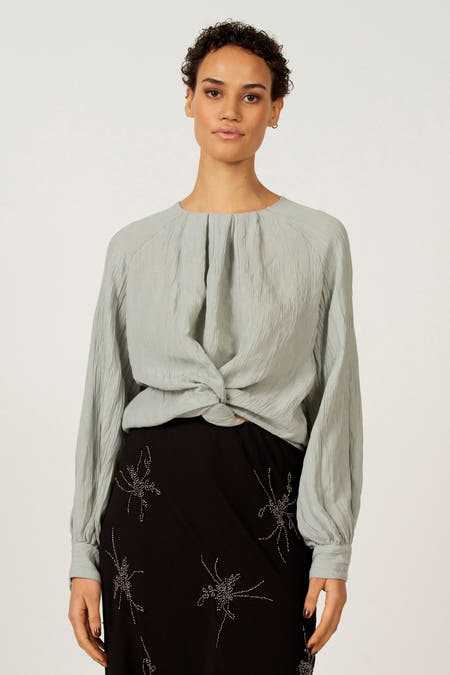 Blouse bleue à longues manches d'Astrid Black Label, boutonnée sur l'avant, portée avec une jupe noire à des décorations scintillantes.