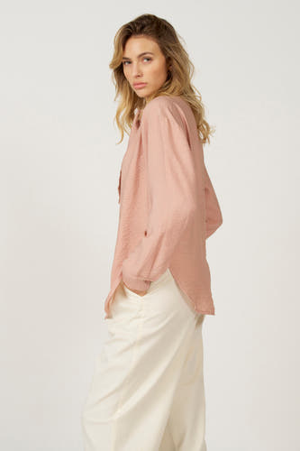 Roze blouse met lange mouwen van Astrid Black Label, met crêpe textuur en gedragen met witte broek.
