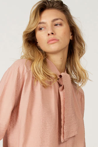 Blouse rose à longues manches d'Astrid Black Label, avec un collier autour du cou.