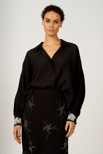 Chemise noire à longues manches d'Astrid Black Label, avec des détails argentés sur la jupe et les cols.
