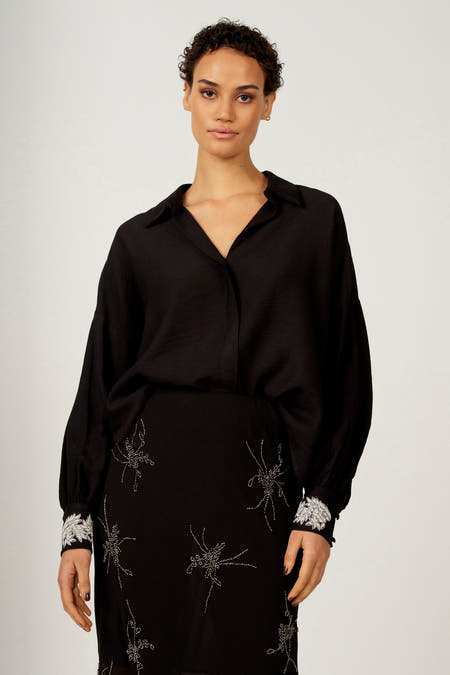 Zwart hemd met lange mouwen van Astrid Black Label, met zilveren sierdetails op de rok en manchetten.
