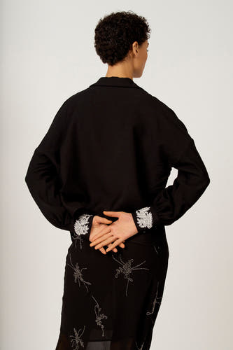 Chemise noire à longues manches d'Astrid Black Label, avec motif de feuille sur les poignets et jupe à motifs floraux.