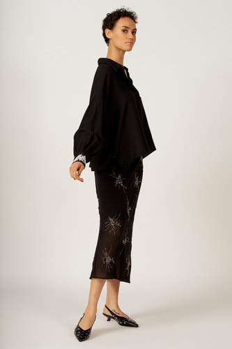 Chemise noire à manches longues d'Astrid Black Label, avec des manchettes brodées, associée à une jupe noire pailletée.