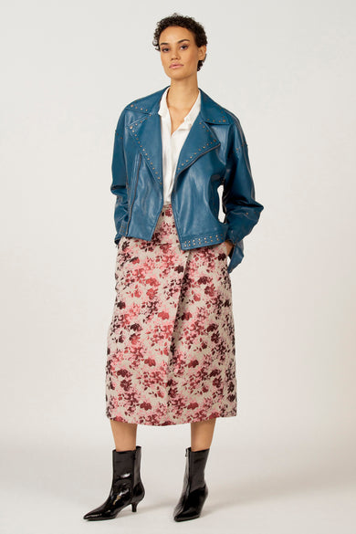 Wit hemd met lange mouwen van Astrid Black Label, gedragen onder een blauw leren jasje met studs, gecombineerd met een gebloemde rok en zwarte laarsjes.

