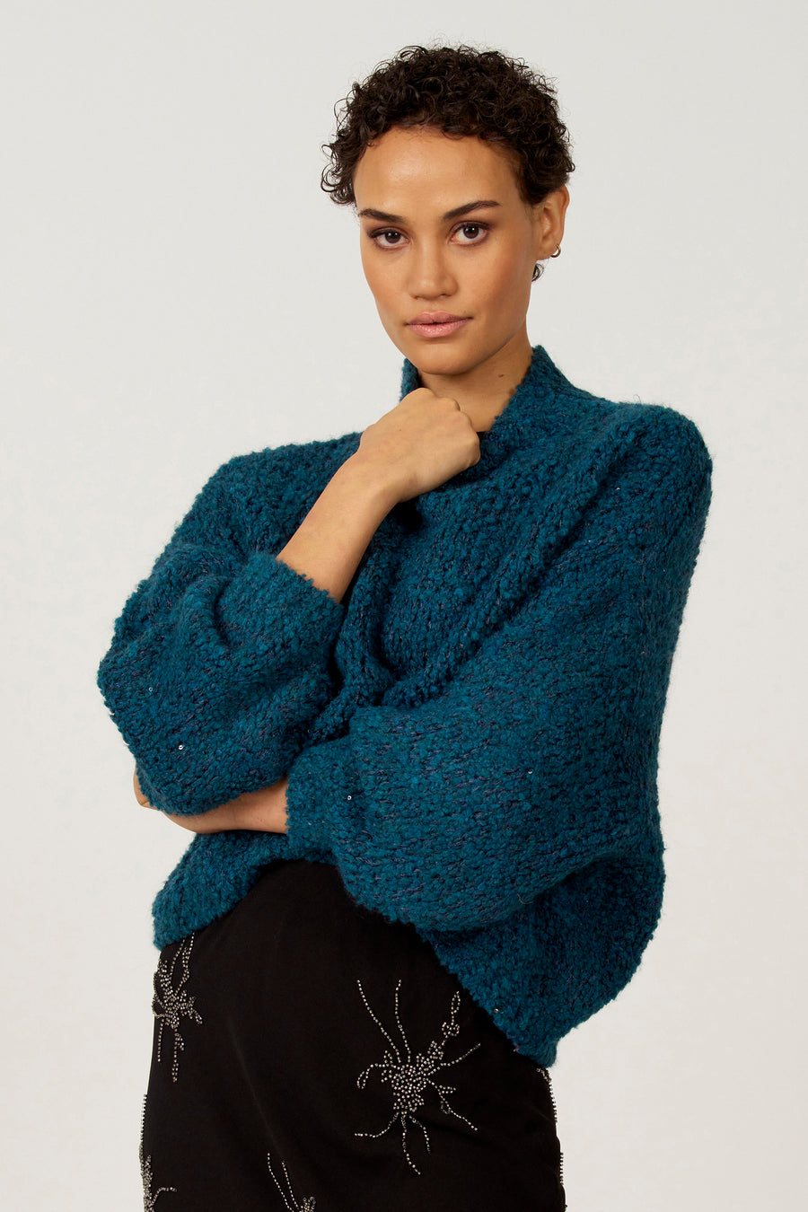 Vrouw draagt blauwgroene, gebreide trui en zwarte rok met versiering.