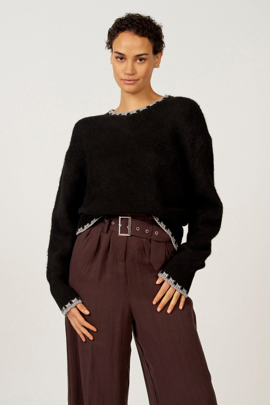 Vrouw in zwarte trui en bruine pantalon met riem.