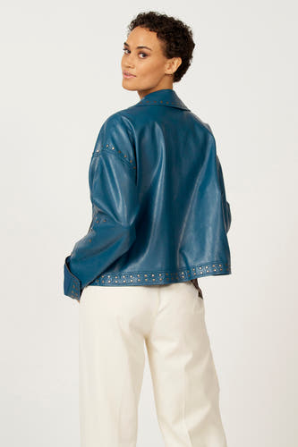 Blauwe leren jas van Astrid Black Label, met zilveren studs, gedragen met een crèmekleurige broek, achteraanzicht.
