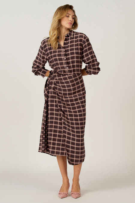 Bruine jurk met lange mouwen van Astrid Black Label, met een geruite patroon, gedragen met roze schoenen met strik.
