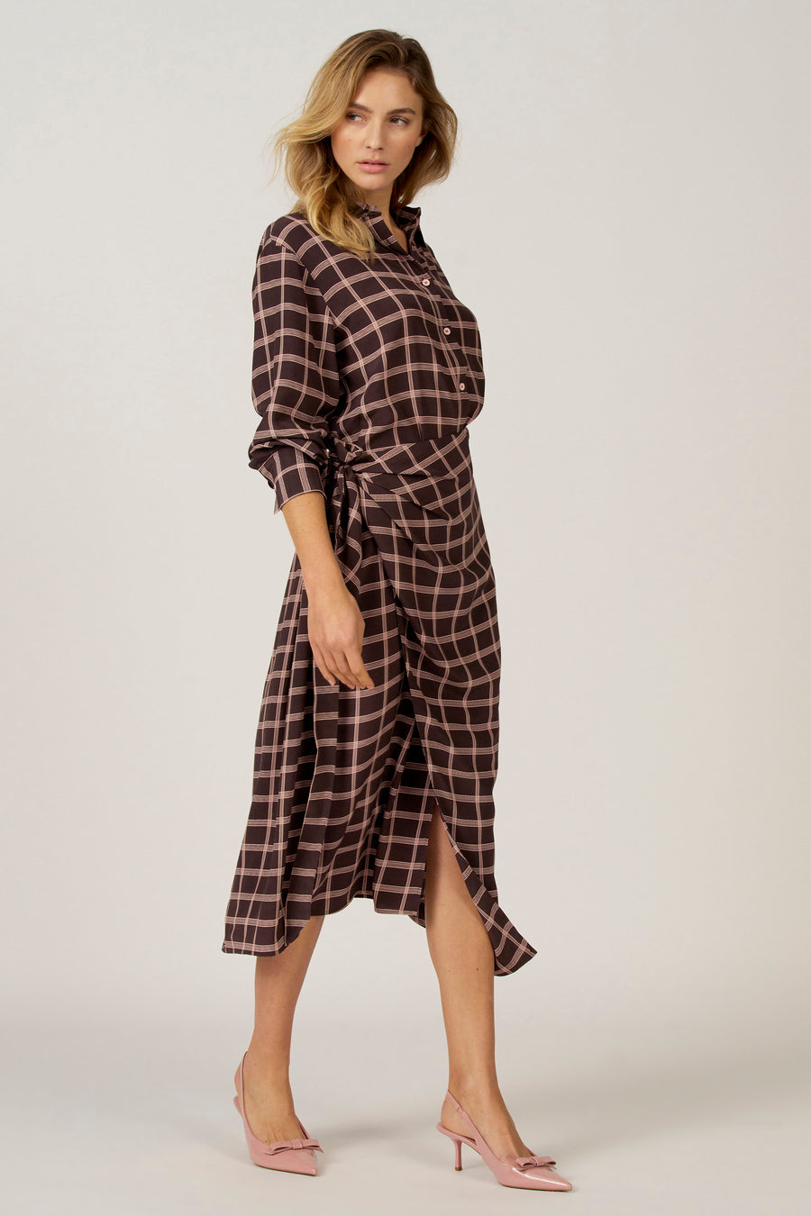 Bruine jurk met lange mouwen van Astrid Black Label, met roze ruitpatroon, overslag en strikdetail.
