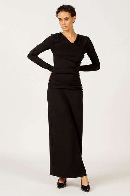 Zwarte jurk met lange mouwen van Astrid Black Label, met gedrapeerd detail en zwarte studschoenen.
