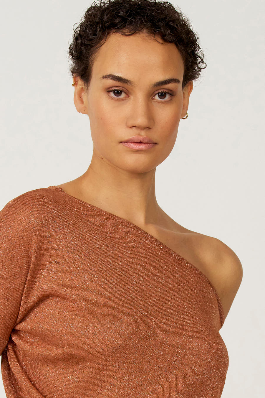 Oranje offshoulder trui van Astrid Black Label, met glanzende textuur en gedragen door een model met een kort kapsel.
