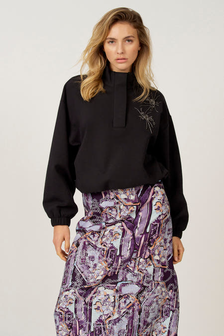 Zwarte sweater van Astrid Black Label met hoge kraag en decoratieve geborduurde details op de schouder.