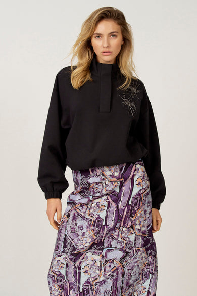 Zwarte sweater van Astrid Black Label met hoge kraag en decoratieve geborduurde details op de schouder.