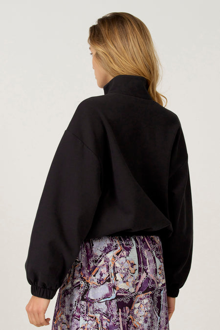 Zwarte sweater van Astrid Black Label, met lange mouwen en een hoge kraag, gecombineerd met een rok met bloemenprint.