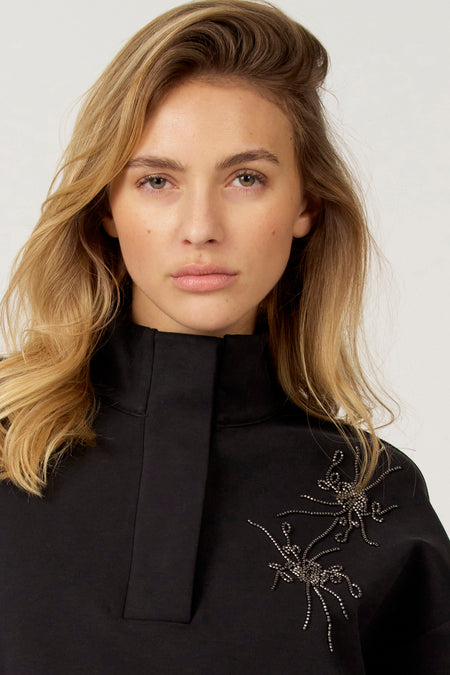 Zwarte trui van Astrid Black Label, met opstaande kraag en decoratieve kralen applicaties.
