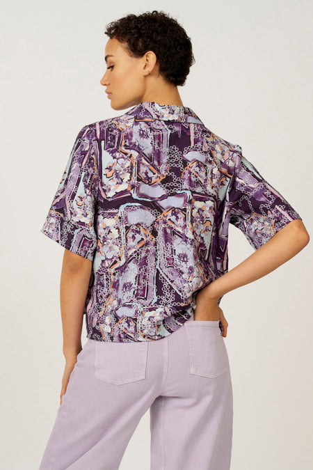 Multikleurige blouse met korte mouwen van Astrid Black Label, met een abstracte paarse print en gedragen met een lila broek.
