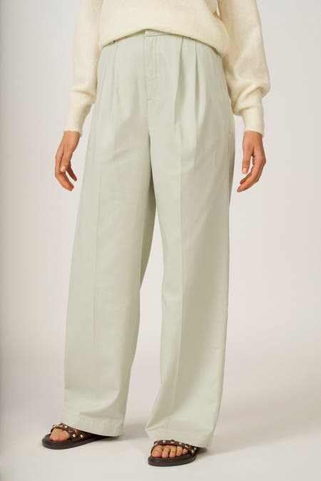 Groene colorbroek van Astrid Black Label, met plooien en wijde pijpen, gecombineerd met een gebreide trui en sandalen.